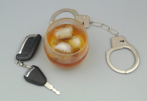 Glass with alcohol, steel handcuffs and car key on gray background. Drunk driving theme.