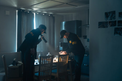 FBI at work at the crime scene. Two agents with a phone and a flashlight, taking pictures of physical evidences on a table, we see them from the distance